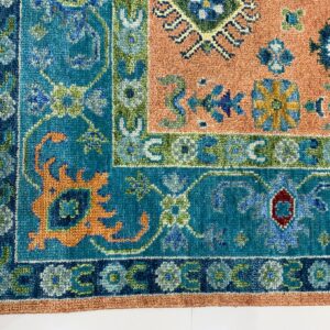 Multicolored rug close-up showing complex floral borders in teal, blue, apricot, and green on white flooring.