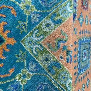Detailed view of a textured rug displaying complex geometric patterns in teal, orange, blue, and green.