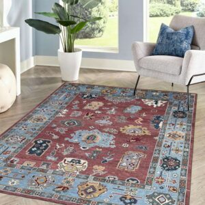 A rust and blue traditional rug with geometric patterns covers herringbone wood floors in a sunny room.