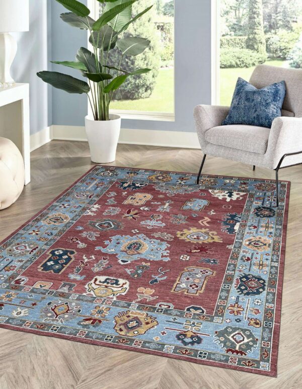 A rust and blue traditional rug with geometric patterns covers herringbone wood floors in a sunny room.