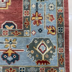 This rug detail shows intricate traditional patterns in red, sky blue, and slate gray on white tile.