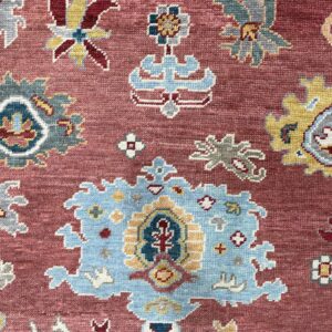A detailed view of a rug showing light blue, gold, and grey traditional motifs on a dusty rose field.