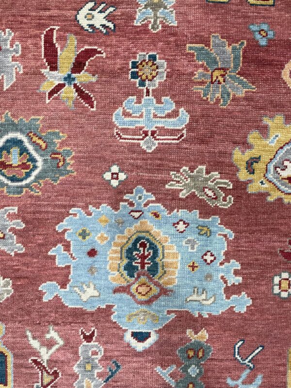 A detailed view of a rug showing light blue, gold, and grey traditional motifs on a dusty rose field.