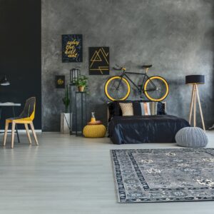Grey and navy traditional rug placed on light flooring in a dark grey bedroom with a desk and bicycle decor.