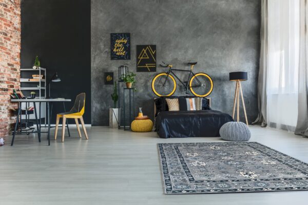 Grey and navy traditional rug placed on light flooring in a dark grey bedroom with a desk and bicycle decor.
