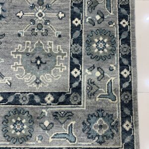 Gray traditional rug corner with detailed navy and light blue geometric patterns on a white tile floor.