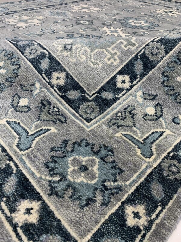 Textured high-pile rug in shades of grey, navy, teal, and cream displays complex traditional floral and geometric patterns.