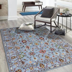 Blue traditional rug with multi-colored floral pattern on light gray wood flooring beside a modern chair.