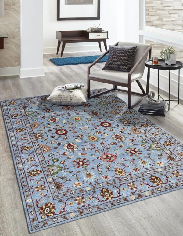 Blue traditional rug with multi-colored floral pattern on light gray wood flooring beside a modern chair.