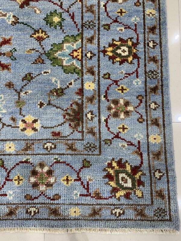 Textured light blue rug with a traditional multi-color floral pattern and dark brown border on white tile.