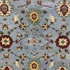 Light blue rug with a dense traditional floral motif in burgundy, gold, teal, and brown.