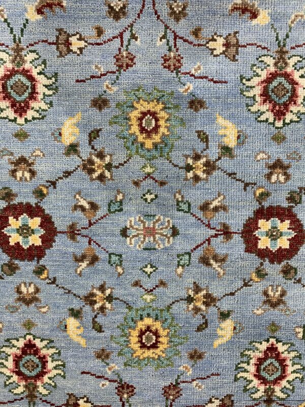 Light blue rug with a dense traditional floral motif in burgundy, gold, teal, and brown.