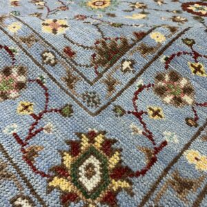 A textured, light blue rug featuring traditional floral and vine patterns in yellow, red, and brown.
