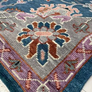 Blue floral rug detail showing a gray medallion, purple border, chunky texture, and white fringe on tile.