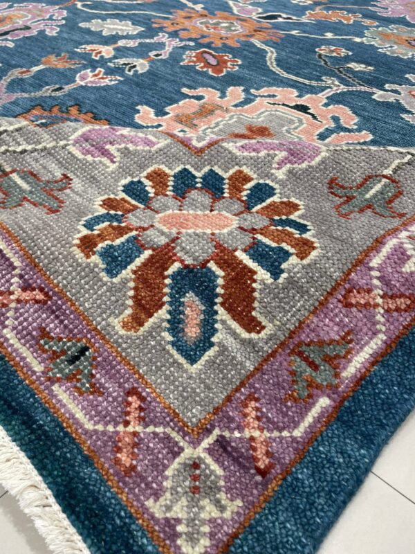 Blue floral rug detail showing a gray medallion, purple border, chunky texture, and white fringe on tile.
