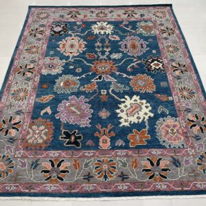Textured, low-pile blue rug with an ornate pattern of orange, pink, purple, and gray flowers on white tile.