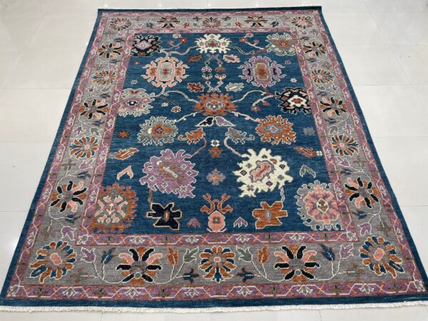 Textured, low-pile blue rug with an ornate pattern of orange, pink, purple, and gray flowers on white tile.
