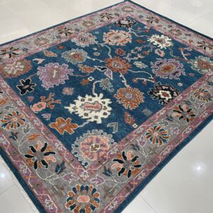 A teal floral rug with rust and purple accents sits on bright, reflective white tile flooring.