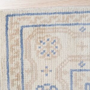 Textured cream and tan rug with light blue geometric borders and motifs sits on light wood flooring.