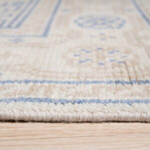 Close-up low-angle view of a thick cream rug with blue geometric patterns on light wood flooring.