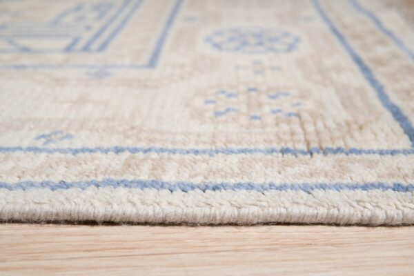 A close profile view of a thick, cream and light blue geometric rug on light wood flooring.