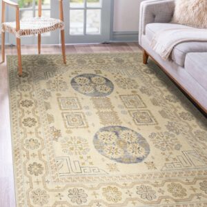A low-pile cream rug with traditional blue and beige patterns sits between a wood chair and gray couch.
