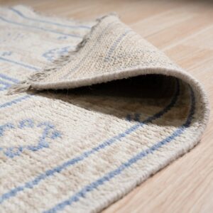 The rolled edge of a cream shag rug with blue geometric lines sits on light wood flooring.
