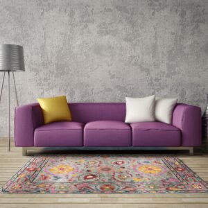 Floral gray and multi-colored rug centered below a bright purple sofa and a silver tripod floor lamp.