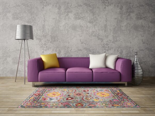 Floral gray and multi-colored rug centered below a bright purple sofa and a silver tripod floor lamp.