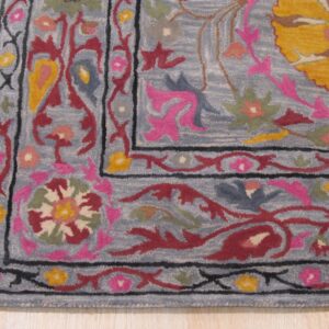 Close-up of a medium-pile rug corner featuring colorful floral patterns on a dusty blue background, resting on light wood flooring.