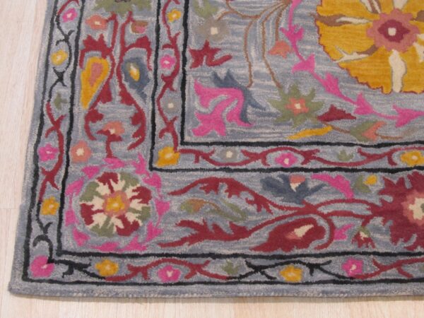 Close-up of a medium-pile rug corner featuring colorful floral patterns on a dusty blue background, resting on light wood flooring.