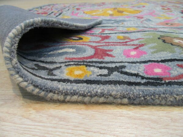 Medium pile blue rug edge, featuring pink, yellow, and green floral motifs, displayed on light wood floor.