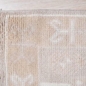 Close-up of a shaggy beige and cream geometric rug with long fringe on light wood flooring.