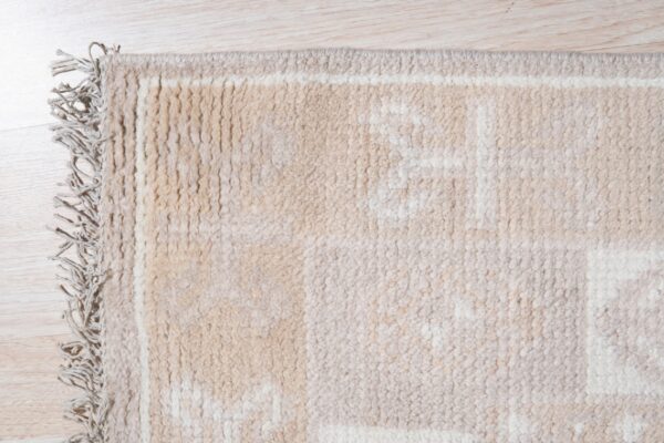Close-up of a shaggy beige and cream geometric rug with long fringe on light wood flooring.