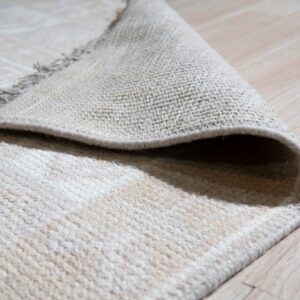 A cream, plush pile rug is folded over, showing its tightly woven backing on light wood flooring.