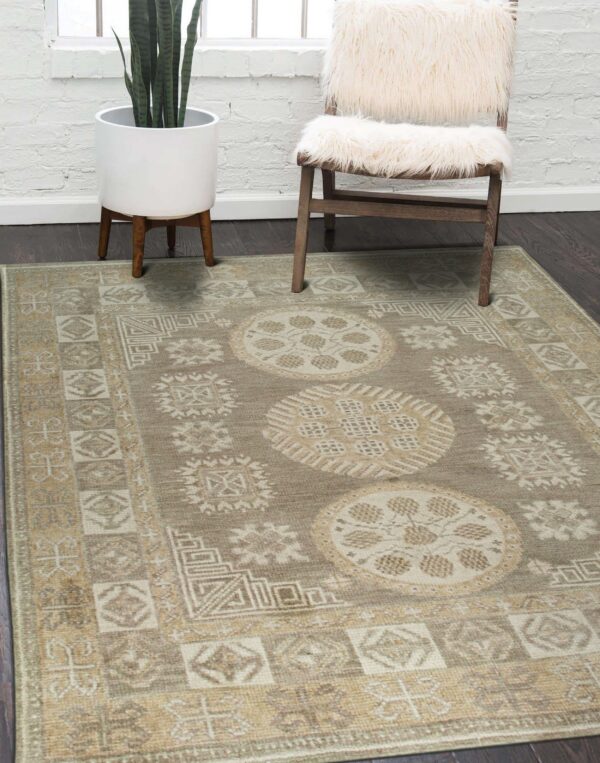 Beige and cream geometric rug on dark wood flooring next to a white furry chair and potted plant.
