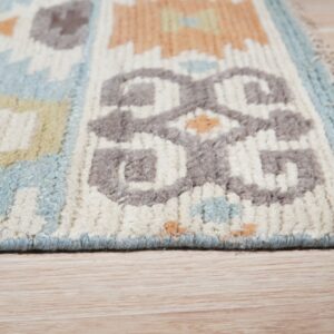 Close-up of a high-pile rug with geometric patterns in blue, cream, gray, and orange on light wooden flooring.