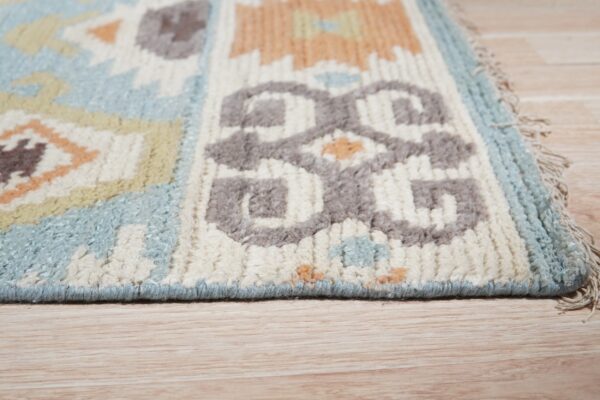 Close-up of a high-pile rug with geometric patterns in blue, cream, gray, and orange on light wooden flooring.