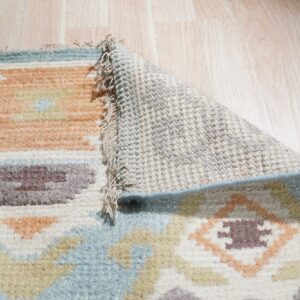 Muted geometric rug pile, woven backing, and fringe are visible against light wood floors.