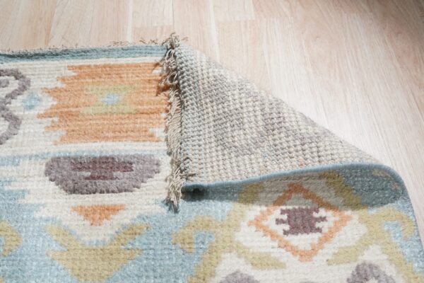 Muted geometric rug pile, woven backing, and fringe are visible against light wood floors.