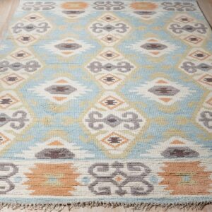 Textured blue and cream geometric rug with gray and orange tribal motifs on light wood flooring.
