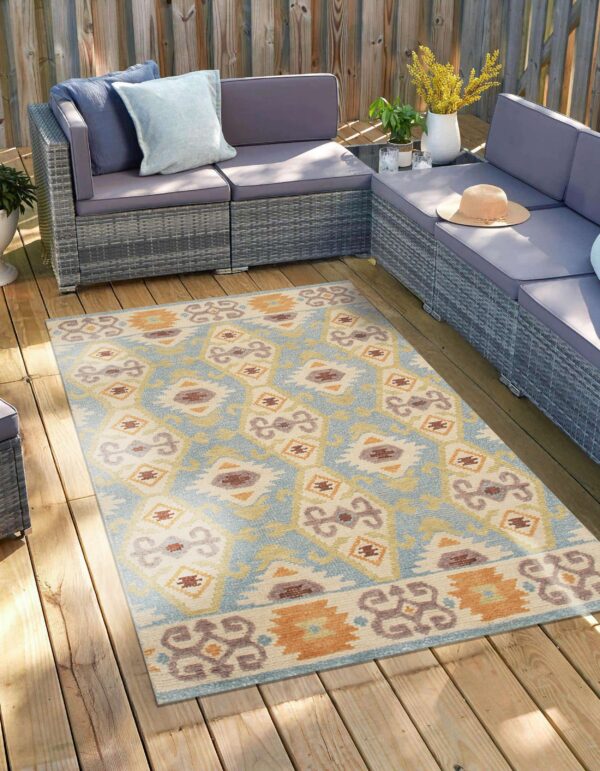 Geometric outdoor rug in shades of blue, cream, and rust accenting a grey patio sectional on a wood deck.