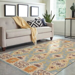 Blue and orange geometric flatweave rug on a gray floor beneath a light beige sofa in a bright room.