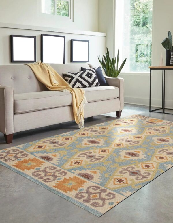 Blue and orange geometric flatweave rug on a gray floor beneath a light beige sofa in a bright room.