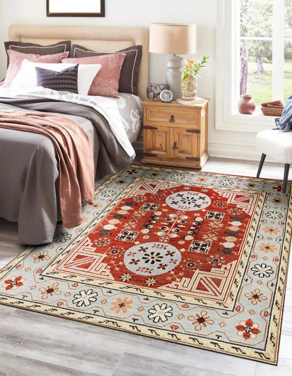 A low-pile rug with a complex red and blue geometric pattern is placed in a brightly lit bedroom.