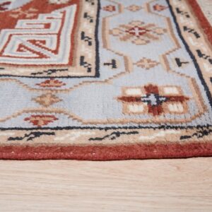 Rust, light blue, and beige geometric rug detail with fringe lying on light wood plank flooring.