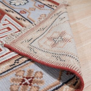 Close-up of a rug with terracotta and pale blue geometric patterns, showing the underside and light wood floor.