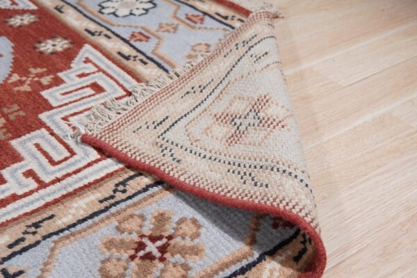 Close-up of a rug with terracotta and pale blue geometric patterns, showing the underside and light wood floor.