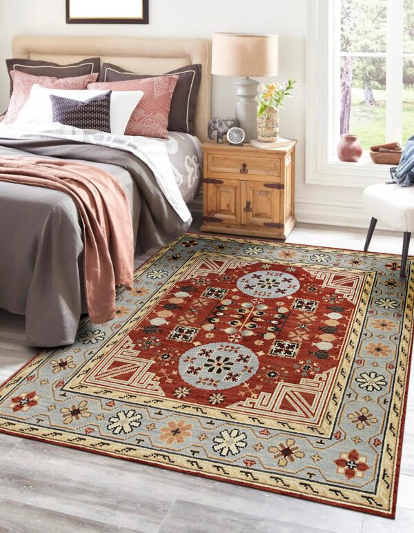 Geometric red, blue, and beige rug placed on gray wood floor beside a bed and nightstand.