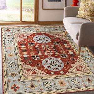 Rust red and blue-gray traditional geometric rug on dark flooring next to a light gray upholstered chair.